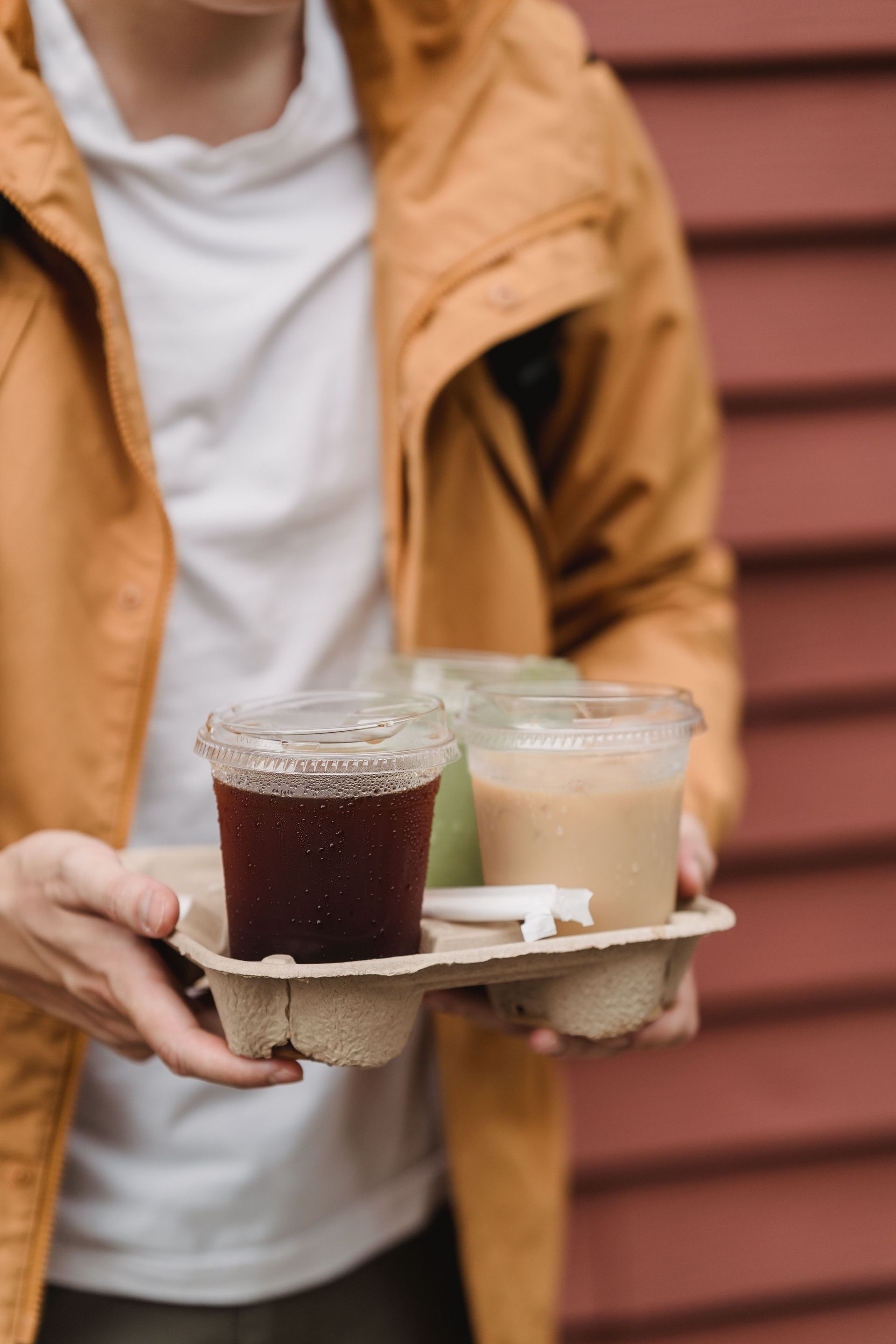 A person carrying a tray with multiple takeout drinks outdoors.